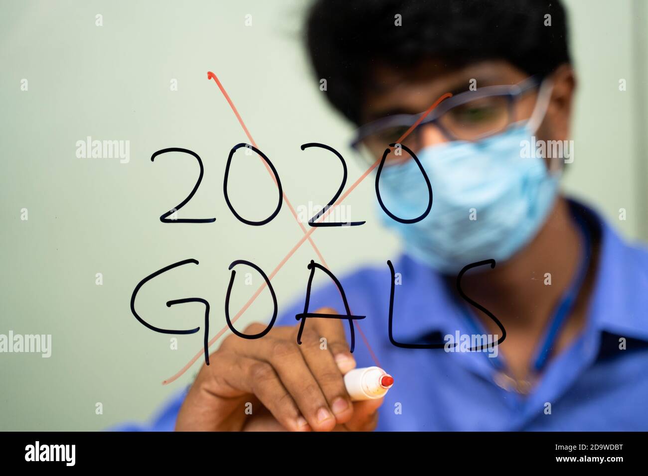 Giovane uomo in maschera medica graffiando 2020 obiettivi a causa di coronavirus o covid-19 pandemia - concetto di fallimento 2020 obiettivi. Foto Stock