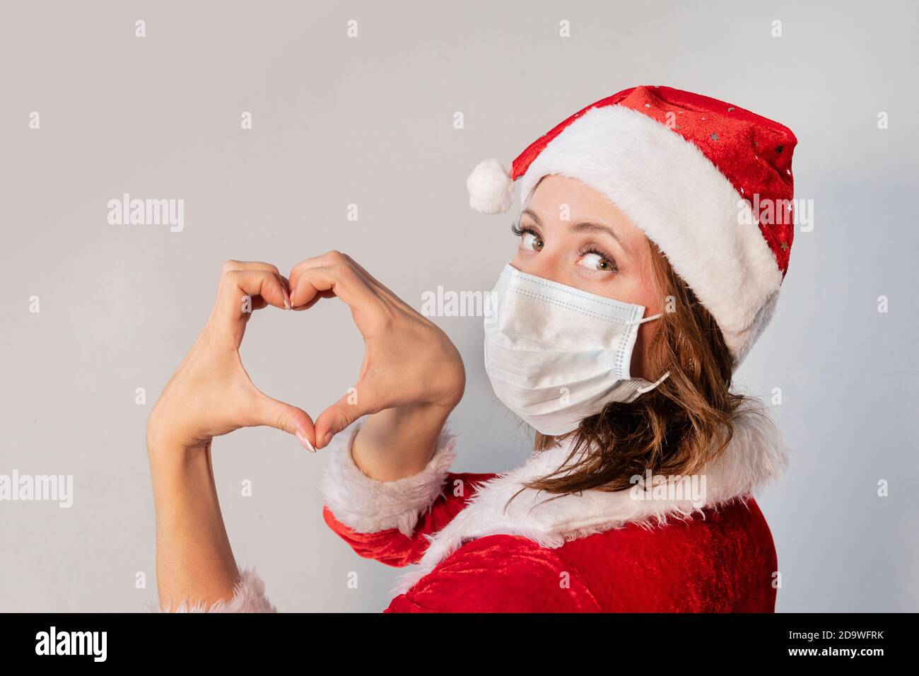 Bella giovane donna in costume rosso di Babbo Natale e maschera medica protettiva contro il virus. Concetto di celebrare il Natale in covid 19 pandemia e. Foto Stock