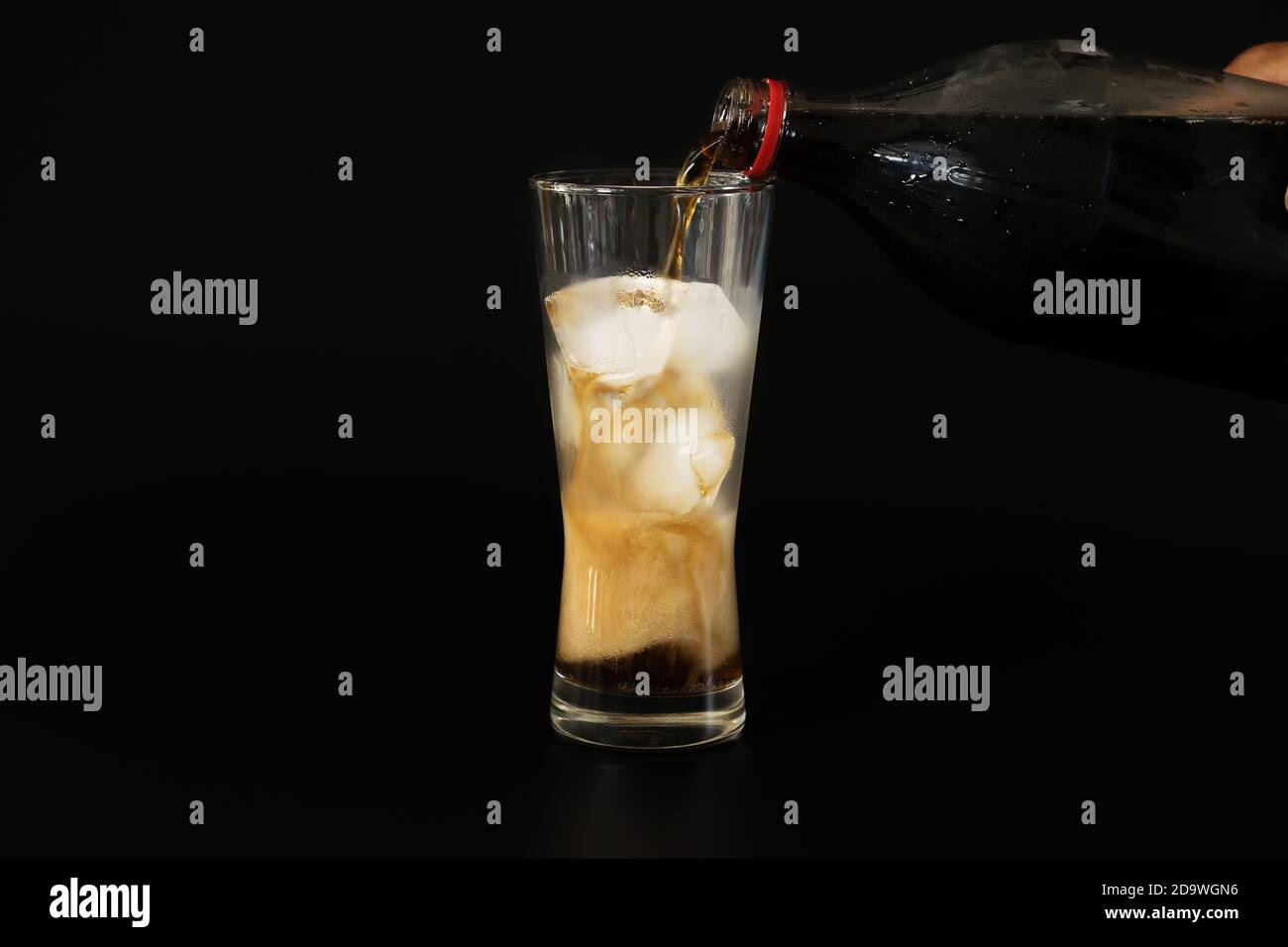Versare la cola da una bottiglia di plastica in un bicchiere di ghiaccio su fondo nero, cibi e bevande. Foto Stock