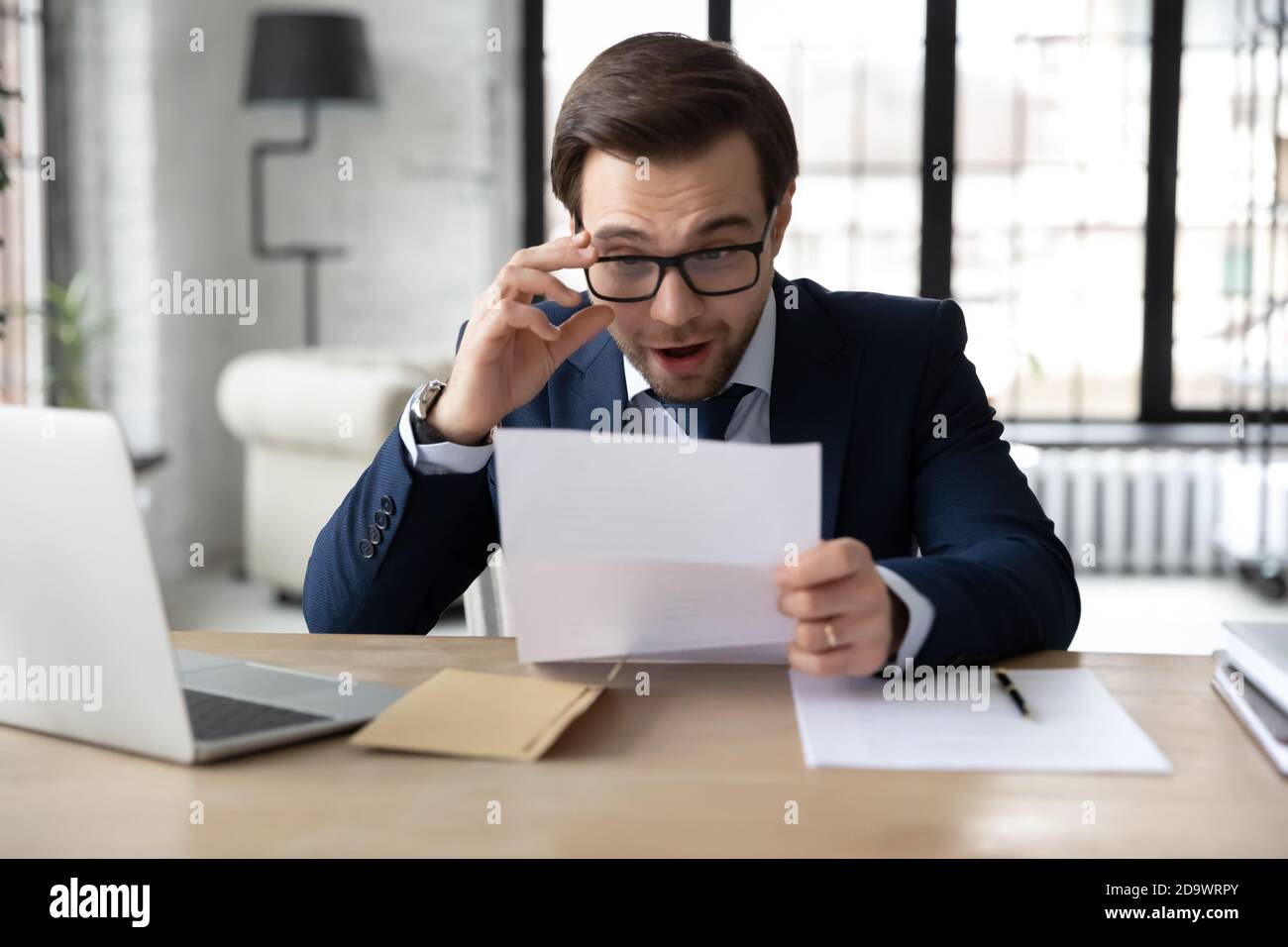 Sorpreso giovane felice uomo d'affari che legge inattesa buone notizie. Foto Stock