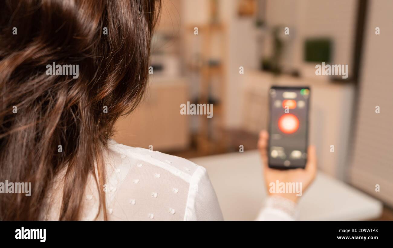 Utilizzo di smartphone con tecnologia per controllare il sistema di illuminazione domestica. Persona in appartamento che tiene il telefono con touchscreen e app per le luci. Foto Stock