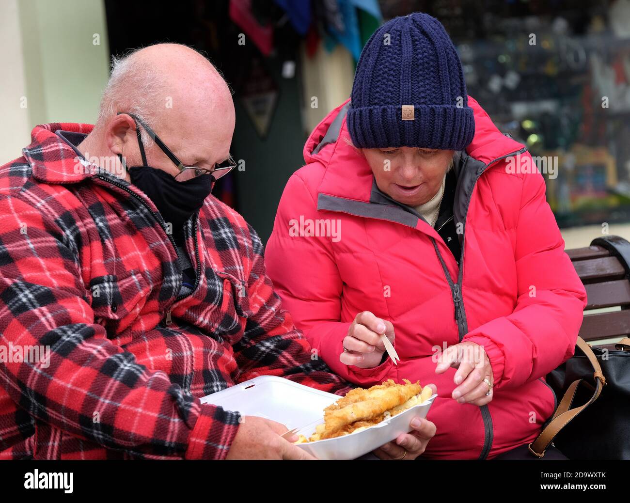 Uomo e donna con vassoio di pesce e patatine da mangiare per strada. REGNO UNITO. Foto Stock