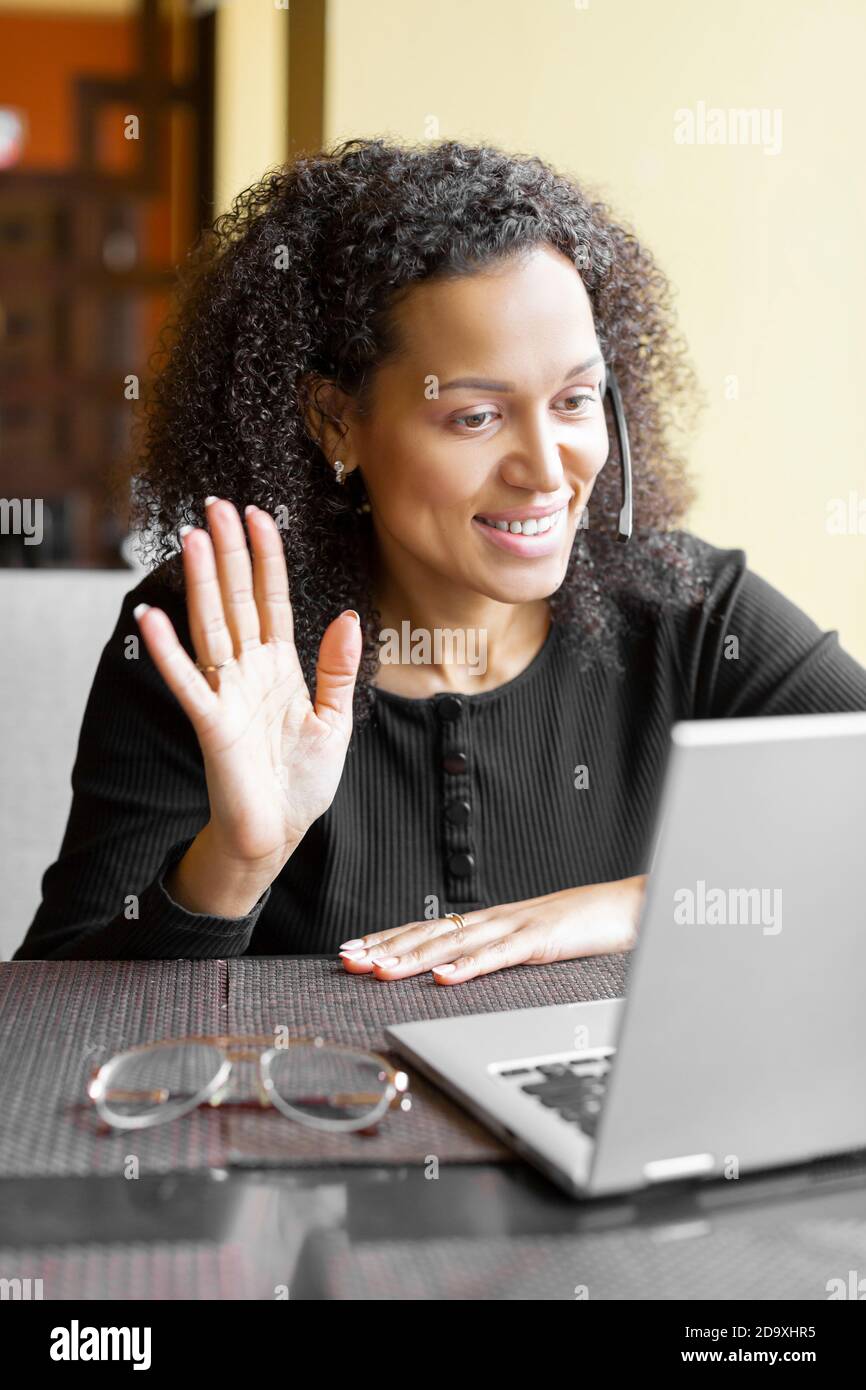 Donna afroamericana in cuffia con conversazione online davanti al monitor del computer portatile. Foto verticale. Foto Stock