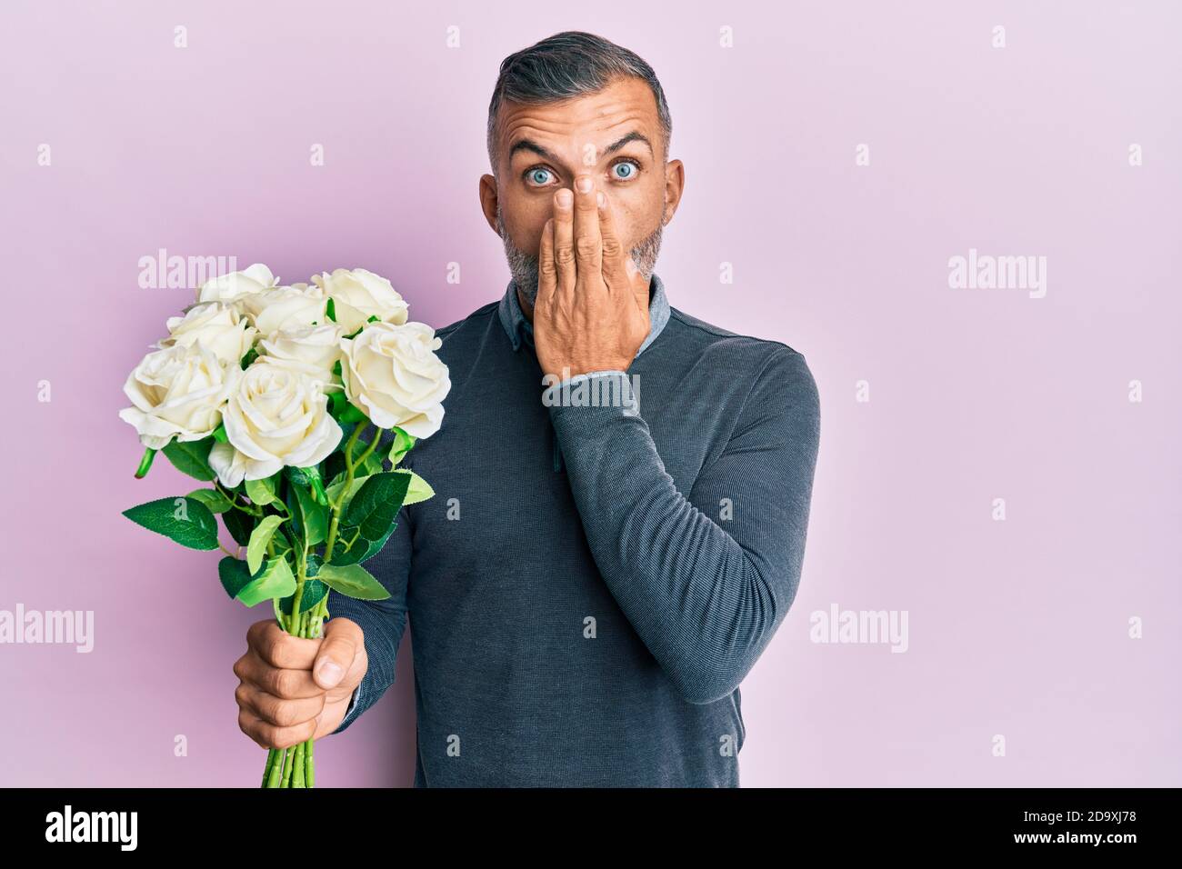 Bell'uomo di mezza età che tiene bouquet di fiori bianchi che coprono la bocca con la mano, scioccato e impaurito per errore. Sorpresa espressione Foto Stock