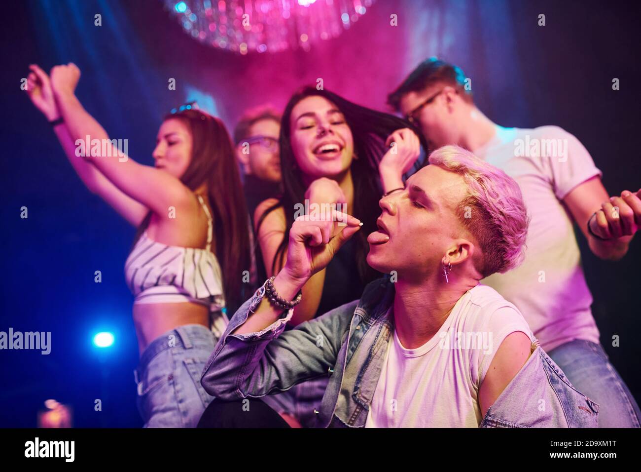 Ragazzo che prende la pillola della droga. I giovani si divertono nel night club con luci laser colorate Foto Stock