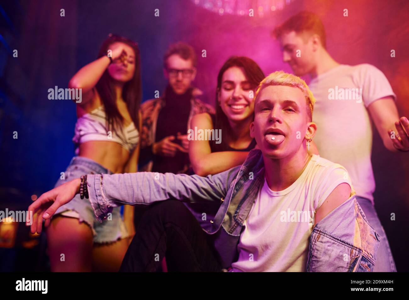 Ragazzo che prende la pillola della droga. I giovani si divertono nel night club con luci laser colorate Foto Stock