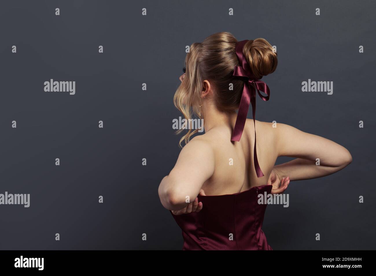 Bella donna che mette su abito da sera setoso su sfondo nero Foto Stock