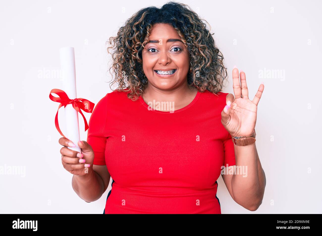 Giovane afroamericano più taglia donna che tiene diploma di laurea facendo segno ok con le dita, sorridente amichevole gesturing eccellente simbolo Foto Stock