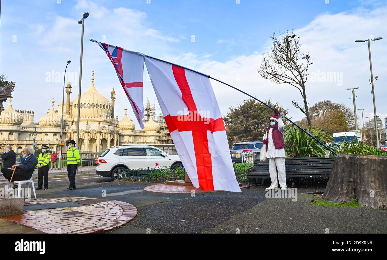 Brighton UK 8 novembre 2020 - un uomo con grandi bandiere guarda il servizio della legge della memoria tenuto al memoriale di guerra della città nel vecchio Steine oggi, dove un piccolo numero di spettatori ha assistito da una distanza a causa delle ultime restrizioni di blocco COVID-19 coronavirus in Inghilterra: Credit Simon Dack / Alamy Live News Foto Stock