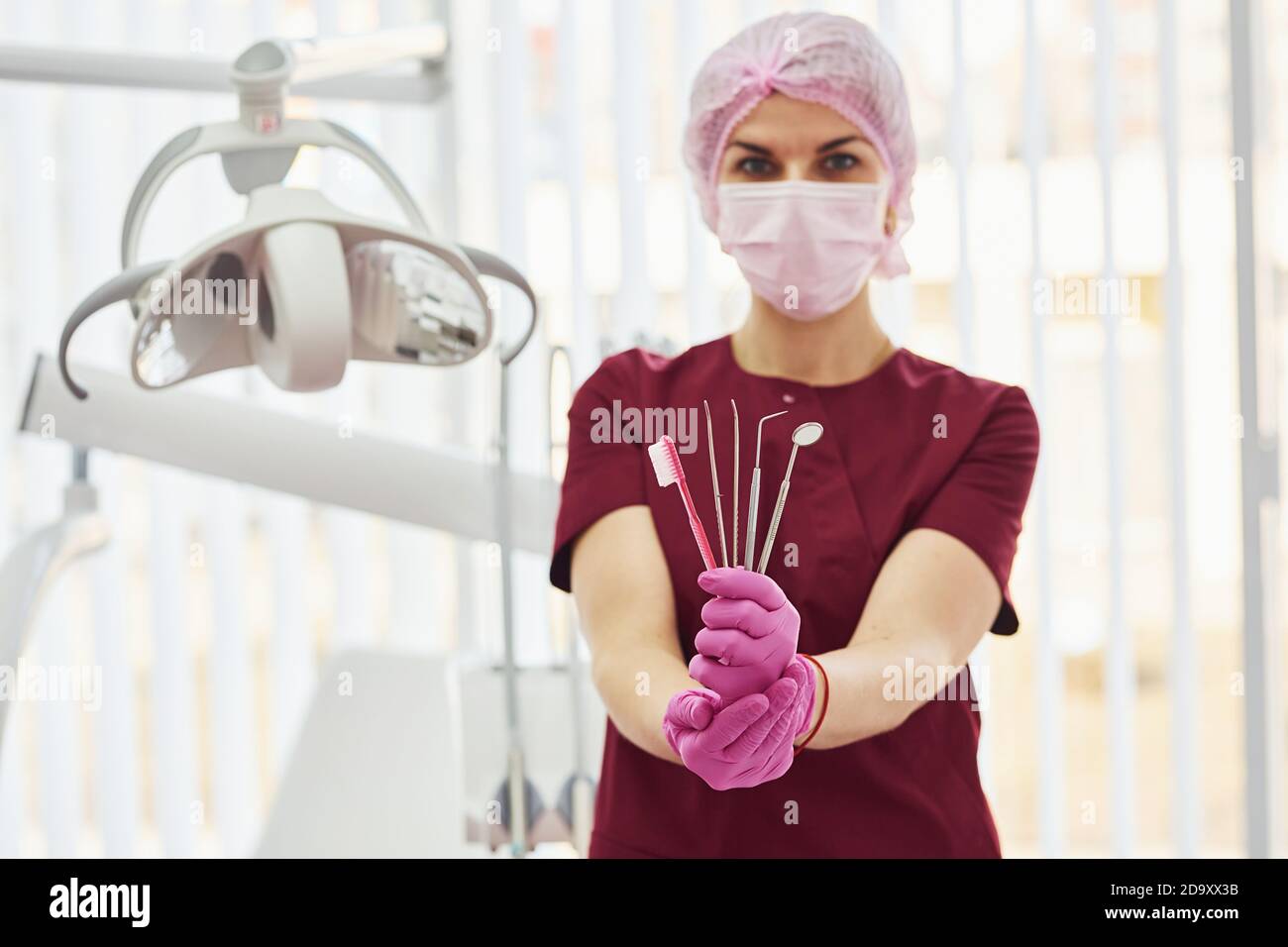 Giovane dentista femminile in piedi uniforme in ufficio di stomatologia, tenendo spazzola e strumenti Foto Stock