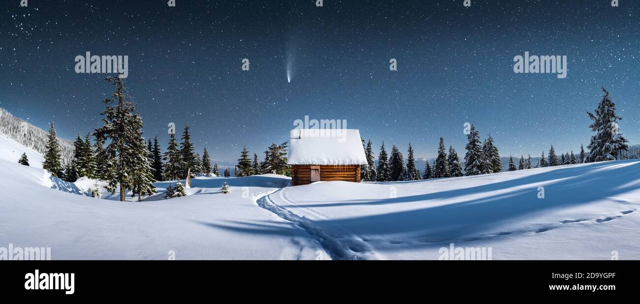 Fantastico panorama invernale con casa in legno in montagne innevate. Cielo stellato con Via Lattea e capanna innevata. Vacanza di Natale e concetto di vacanza invernale Foto Stock