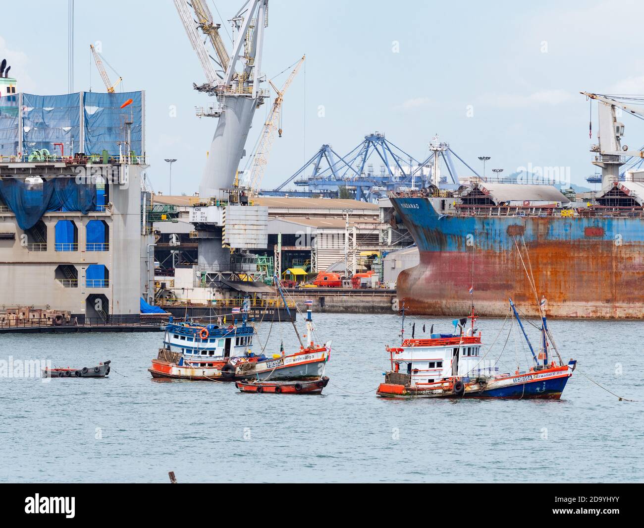 Tradizionali barche da pesca in legno ancorate di fronte ad un grande cantiere navale a Laem Chabang, il più importante porto commerciale della Thailandia. Foto Stock