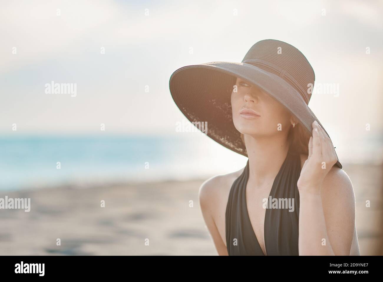 Una donna con un cappello sulla testa che guarda fuori al mare Foto Stock