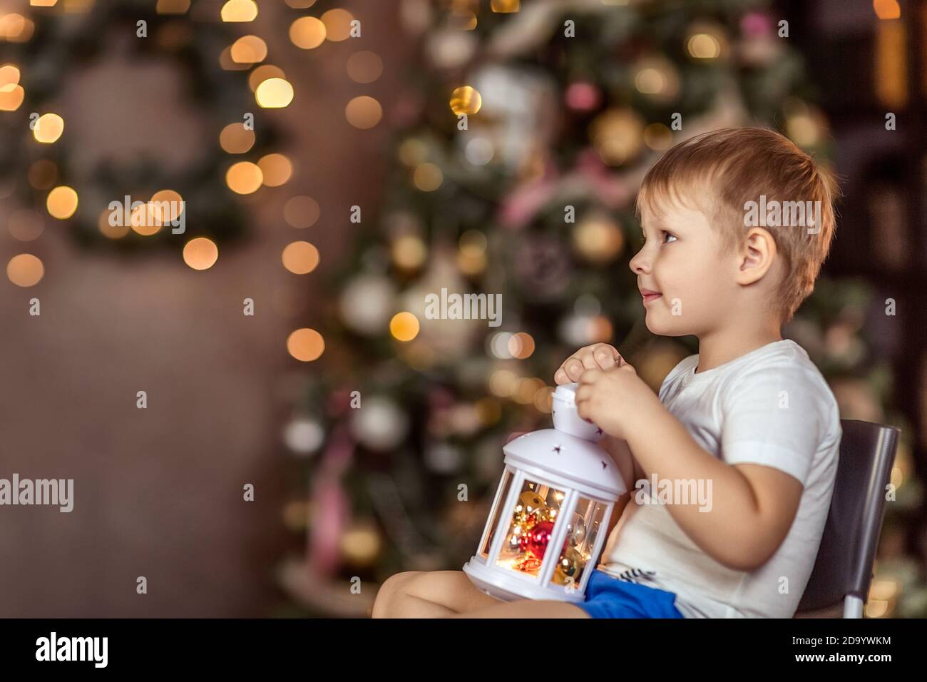 Un bel ragazzo di 4-5 anni è seduto vicino all'albero di Natale. Tiene una torcia scintillante nelle mani e fa un desiderio. Il concetto di Th Foto Stock