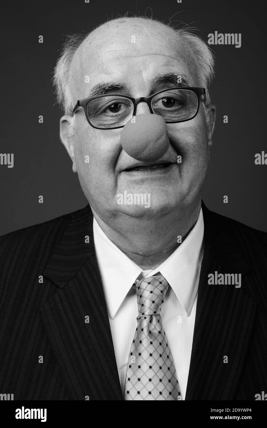 Uomo d'affari anziano in sovrappeso che indossa il naso di clown su sfondo marrone Foto Stock
