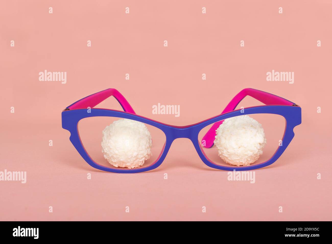 Le palline di Raffaello giacciono dietro lenti di occhiali colorati, su sfondo rosa. Foto Stock