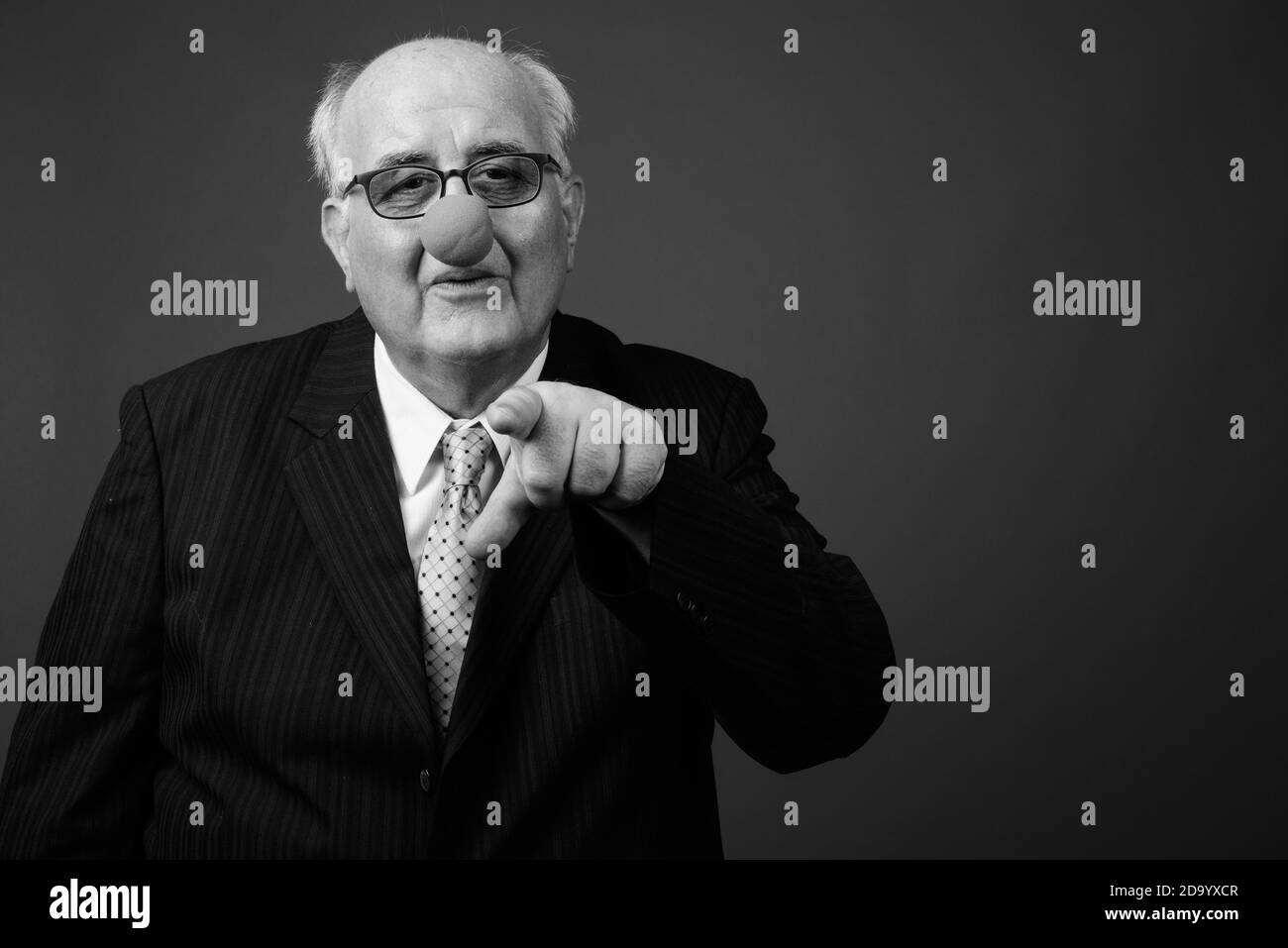 Uomo d'affari anziano in sovrappeso che indossa il naso di clown su sfondo marrone Foto Stock