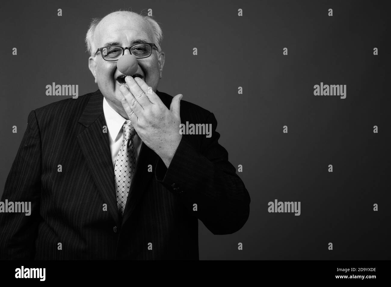 Uomo d'affari anziano in sovrappeso che indossa il naso di clown su sfondo marrone Foto Stock