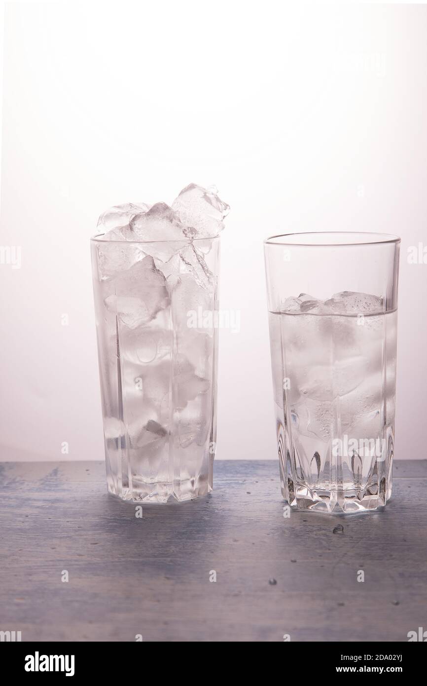 Il concetto di fusione del ghiaccio. Un bicchiere pieno di ghiaccio, l'altra metà piena di acqua. Orientamento verticale Foto Stock