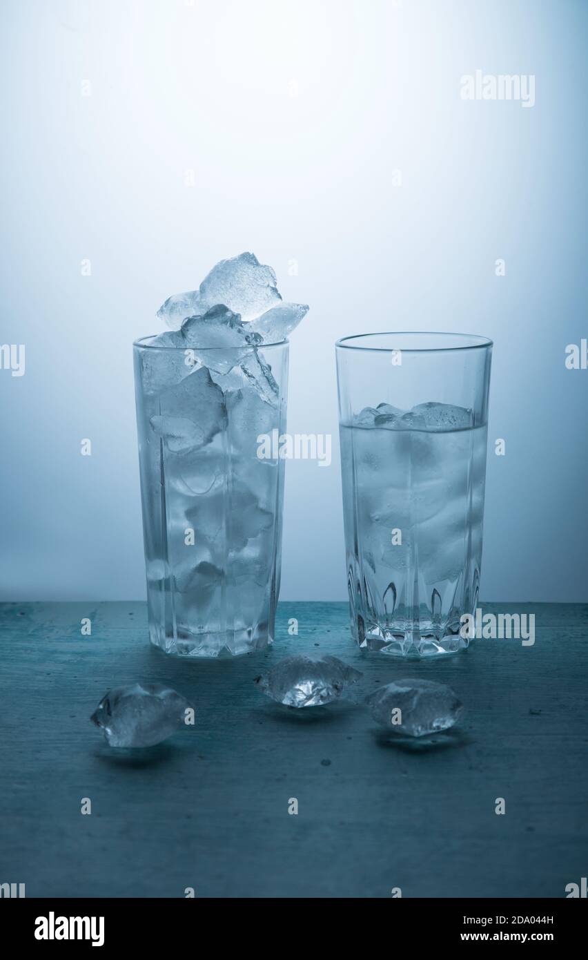 Il concetto di fusione del ghiaccio. Due bicchieri su sfondo blu, un bicchiere pieno di ghiaccio, l'altra metà con acqua. Orientamento verticale Foto Stock