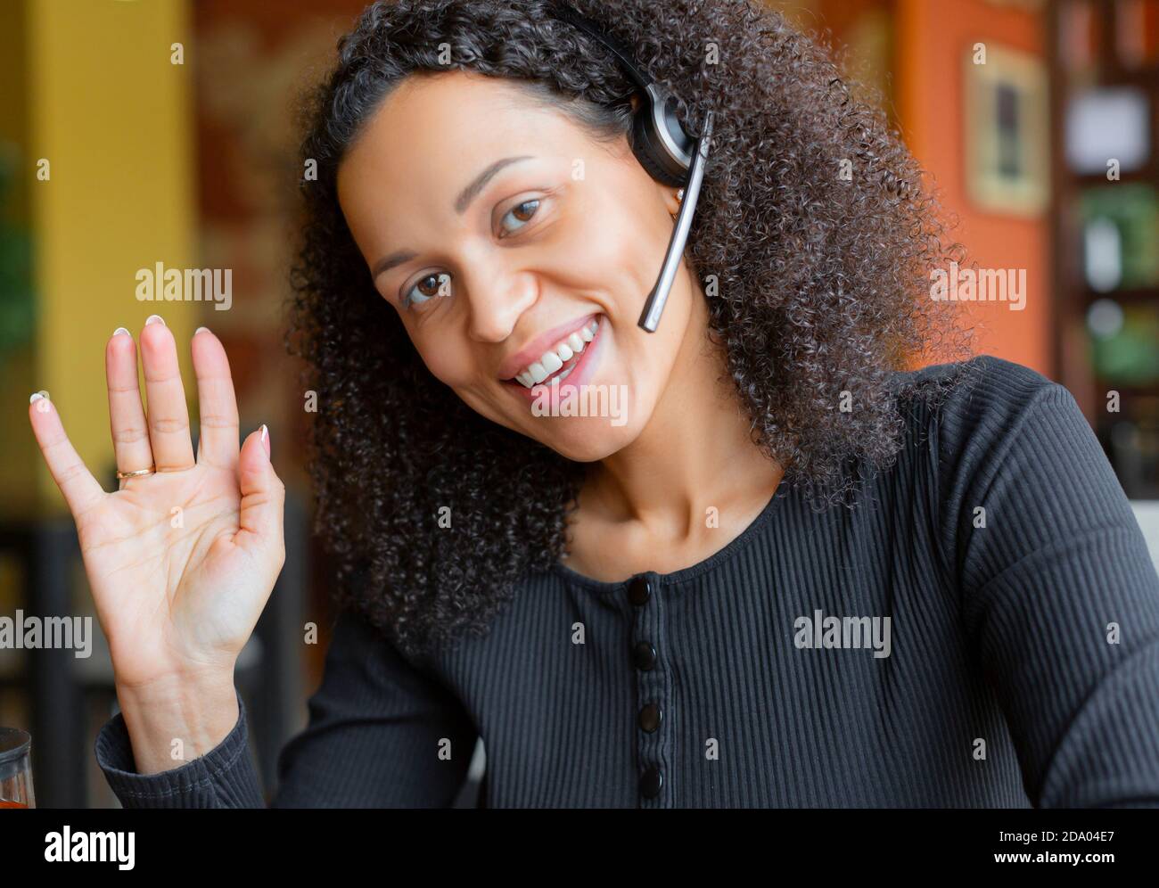 Donna afroamericana in cuffia con conversazione online davanti al monitor del computer portatile. Foto verticale. Guarda la macchina fotografica. Foto Stock