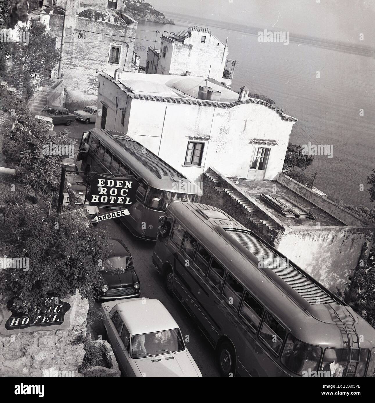 1970, storico, fuori dall'Eden Roc Hotel e affacciato sul Mar Tirreno, le auto passano davanti ai pullman turistici parcheggiati sulla stretta strada di montagna di Positano, sulla popolare costiera amalfitana, Italia. Foto Stock