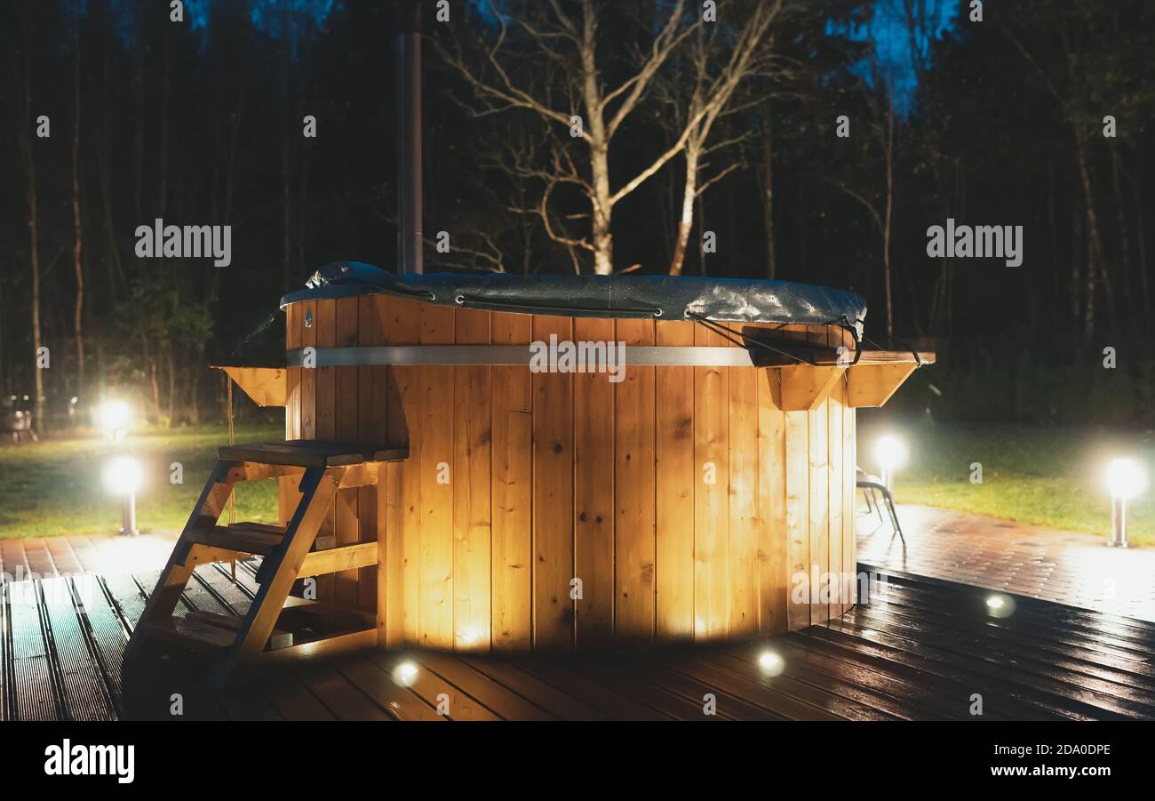 Vasca idromassaggio in legno con caminetto di notte. Foto Stock