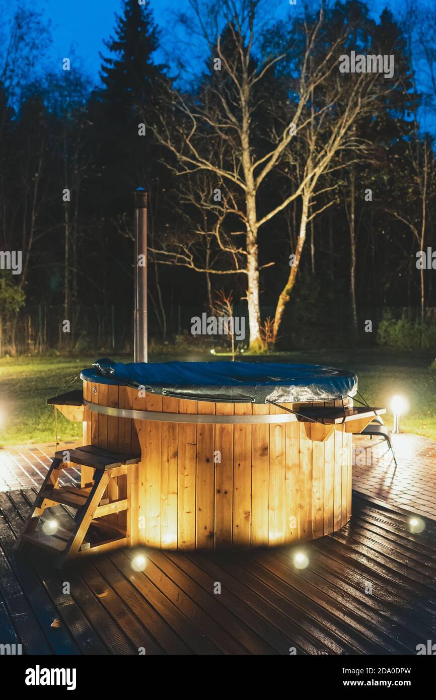 Vasca idromassaggio in legno con caminetto di notte. Foto Stock