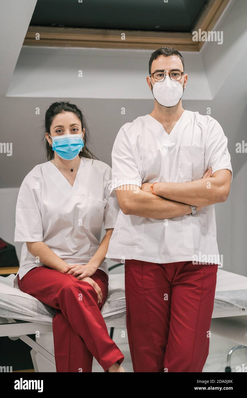 Medici allegri in uniforme e maschera in piedi con braccia incrociate in ospedale moderno e guardando la macchina fotografica Foto Stock