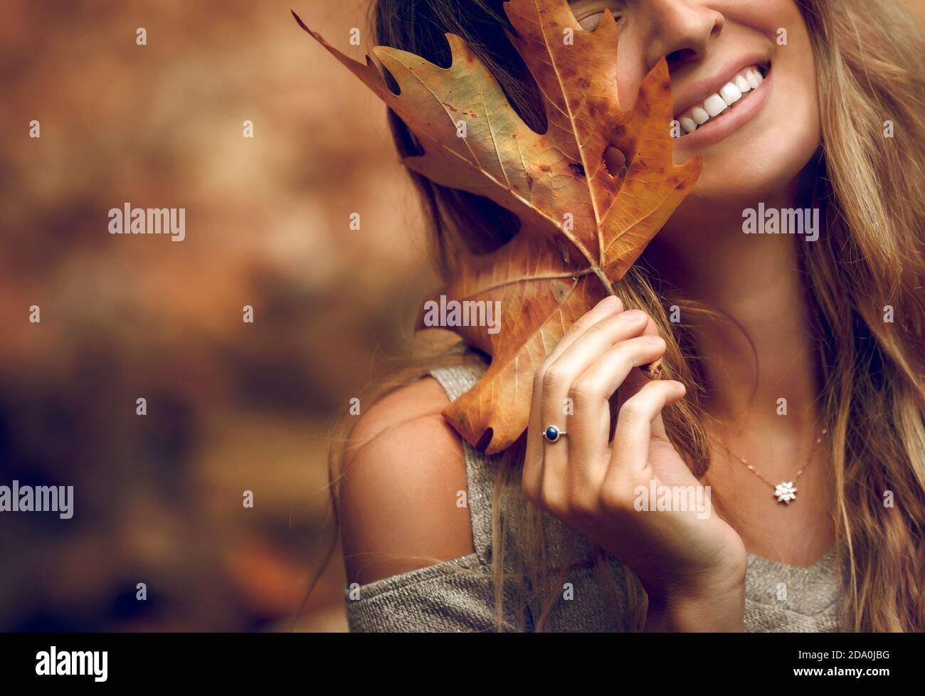 Closeup Ritratto di una donna Pretty che copre il suo viso con foglia di acero secco. Parte faccia. Buone feste d'autunno. Bellezza della natura autunnale. Foto Stock