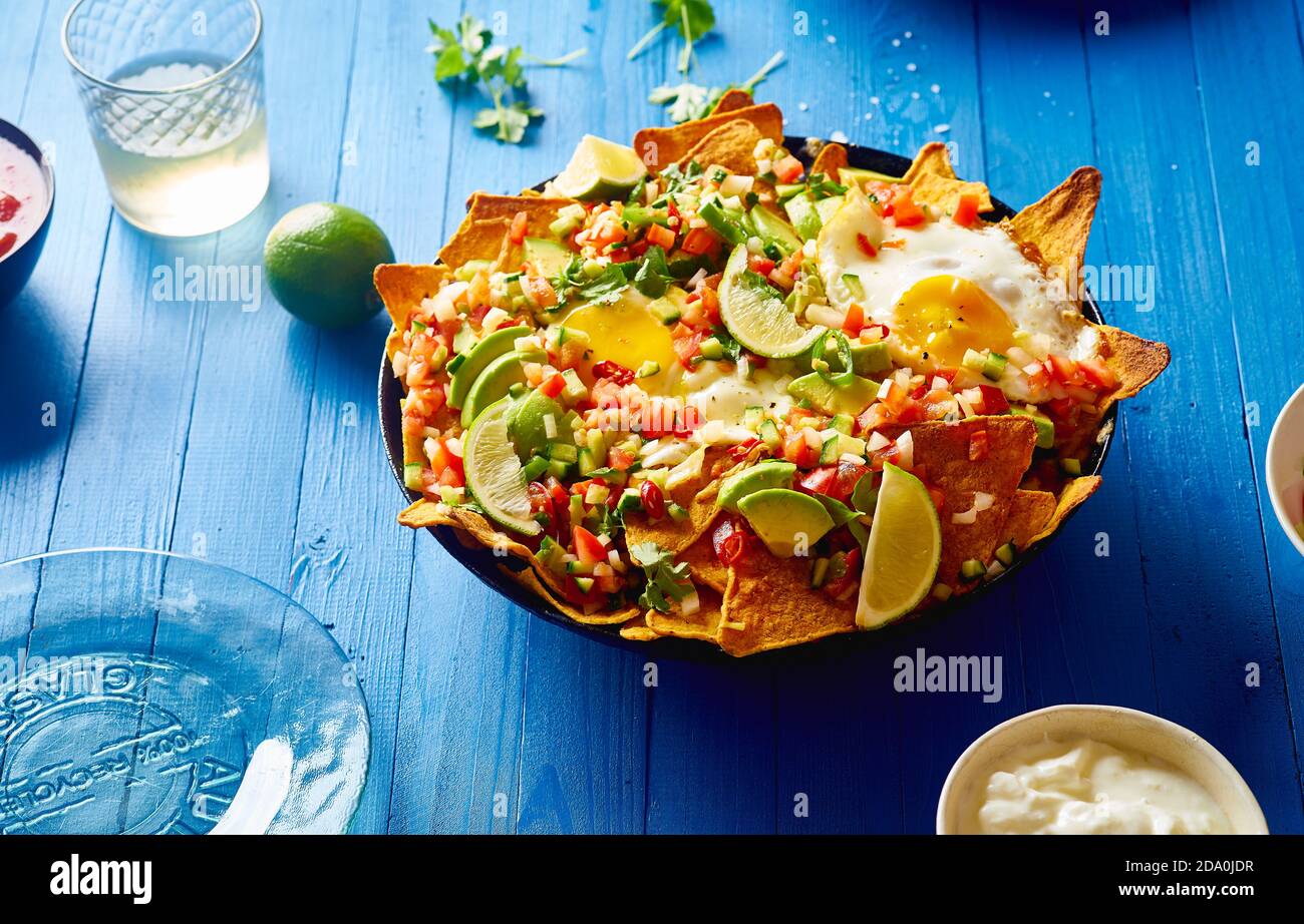 Chilaquiles - colazione messicana fatta di fagioli neri, mais, patatine di tortilla e uova fritte su tavolo di legno blu Foto Stock