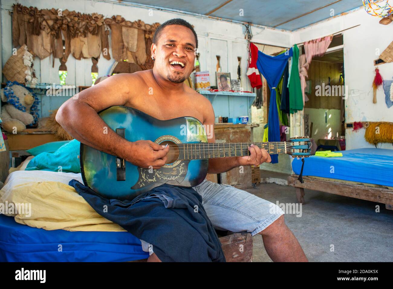 All'interno di una casa tradizionale a Rangiroa, Isole Tuamotus, Polinesia Francese, Sud Pacifico. Uomo che suona la chitarra e cantare con la sua famiglia. Foto Stock