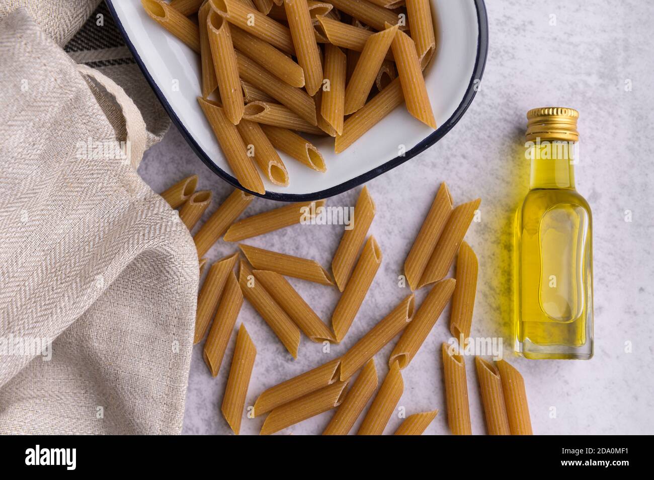 Dall'alto di Penne essiccato in recipiente metallico e. bottiglia di olio d'oliva vergine disposta su tavola con tovagliolo in cucina Foto Stock