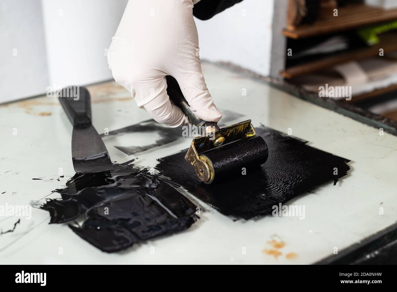 Mano closeup di raccolto anonimo artigiano in guanto con il coraggio e stendendo inchiostro su foglio per incidere mentre si lavora officina professionale Foto Stock