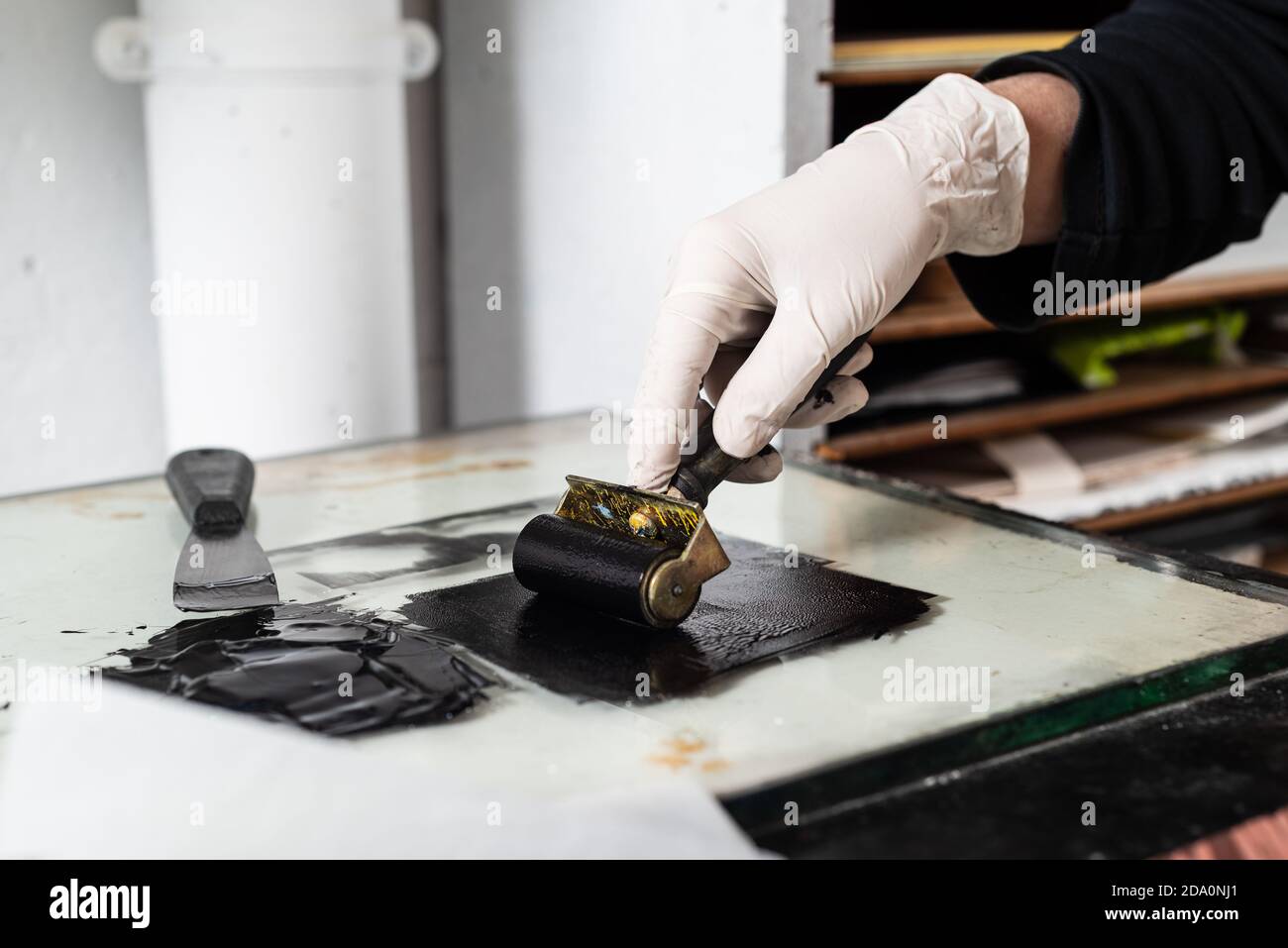 Mano closeup di raccolto anonimo artigiano in guanto con il coraggio e stendendo inchiostro su foglio per incidere mentre si lavora officina professionale Foto Stock