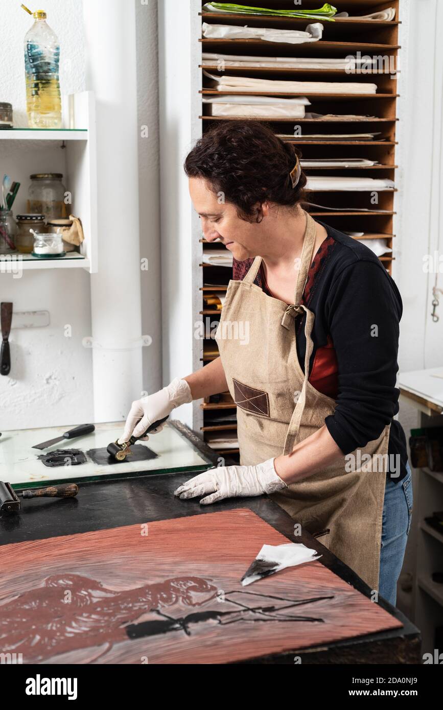 Donna artigiana in guanto con treccia e spalmatura dell'inchiostro foglio per incisione durante il lavoro in officina professionale Foto Stock