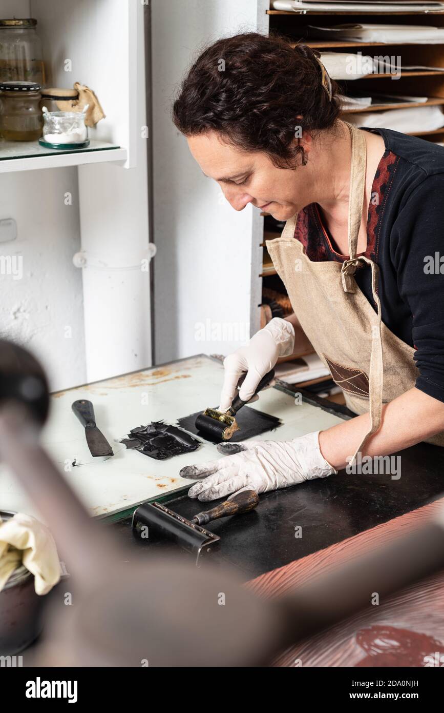 Donna artigiana in guanto con treccia e spalmatura dell'inchiostro foglio per incisione durante il lavoro in officina professionale Foto Stock