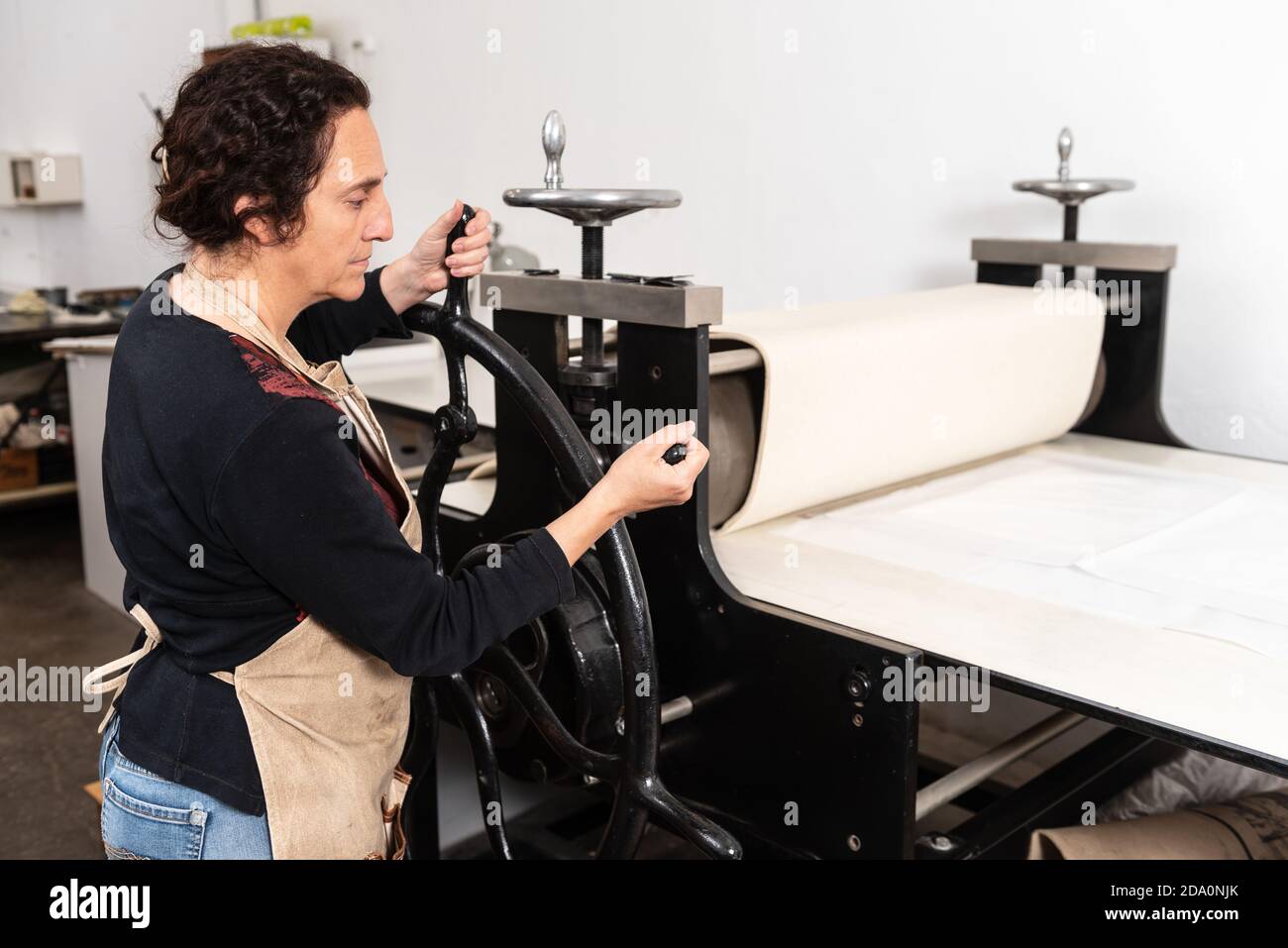 Vista laterale della ruota di filatura artigianale femminile della pressa da stampa macchina mentre si fa l'opera d'arte in tecnica di linocut in officina Foto Stock