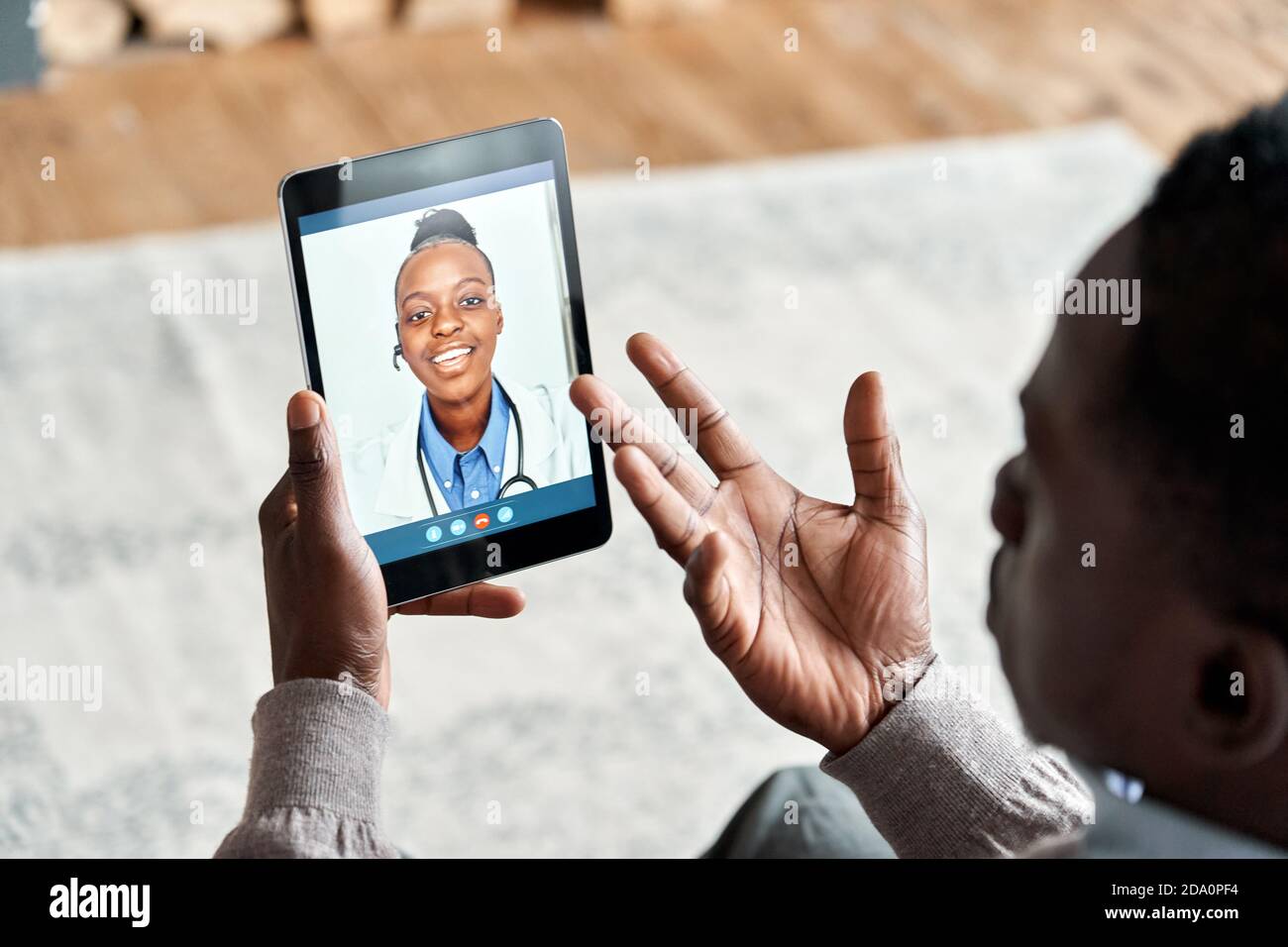 Vista a spalla di un paziente africano che videochiama un medico virtuale su un tablet. Foto Stock