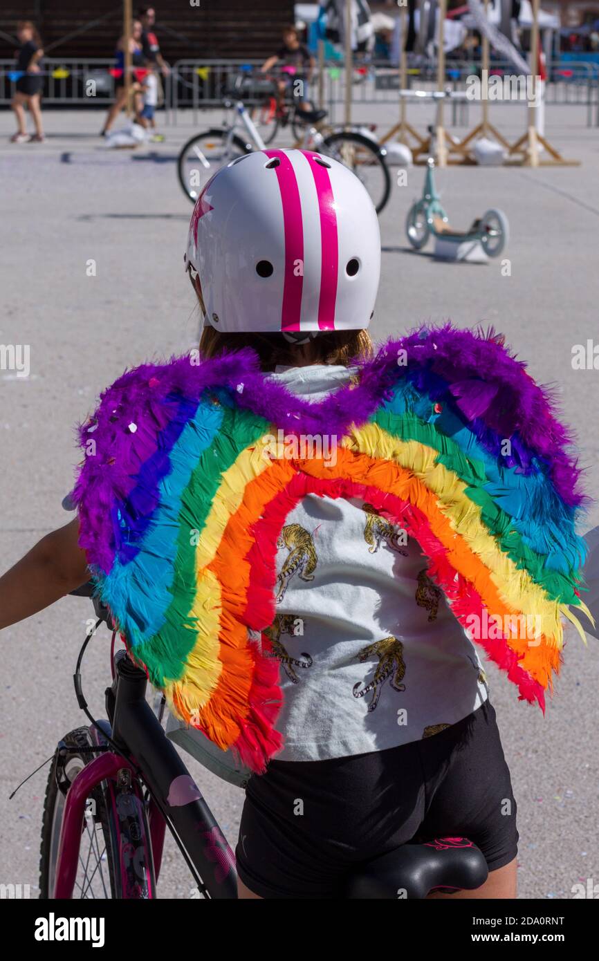 Ragazza con le ali dell'angelo arcobaleno e un casco seduto su una bicicletta guardando una bicicletta elettrica e uno scooter dato come premio. Foto Stock