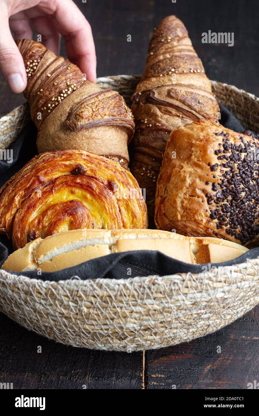 Crop persona con cestino pieno di deliziosi croissant fatti in casa e. mazzi su tavolo di legno a casa Foto Stock