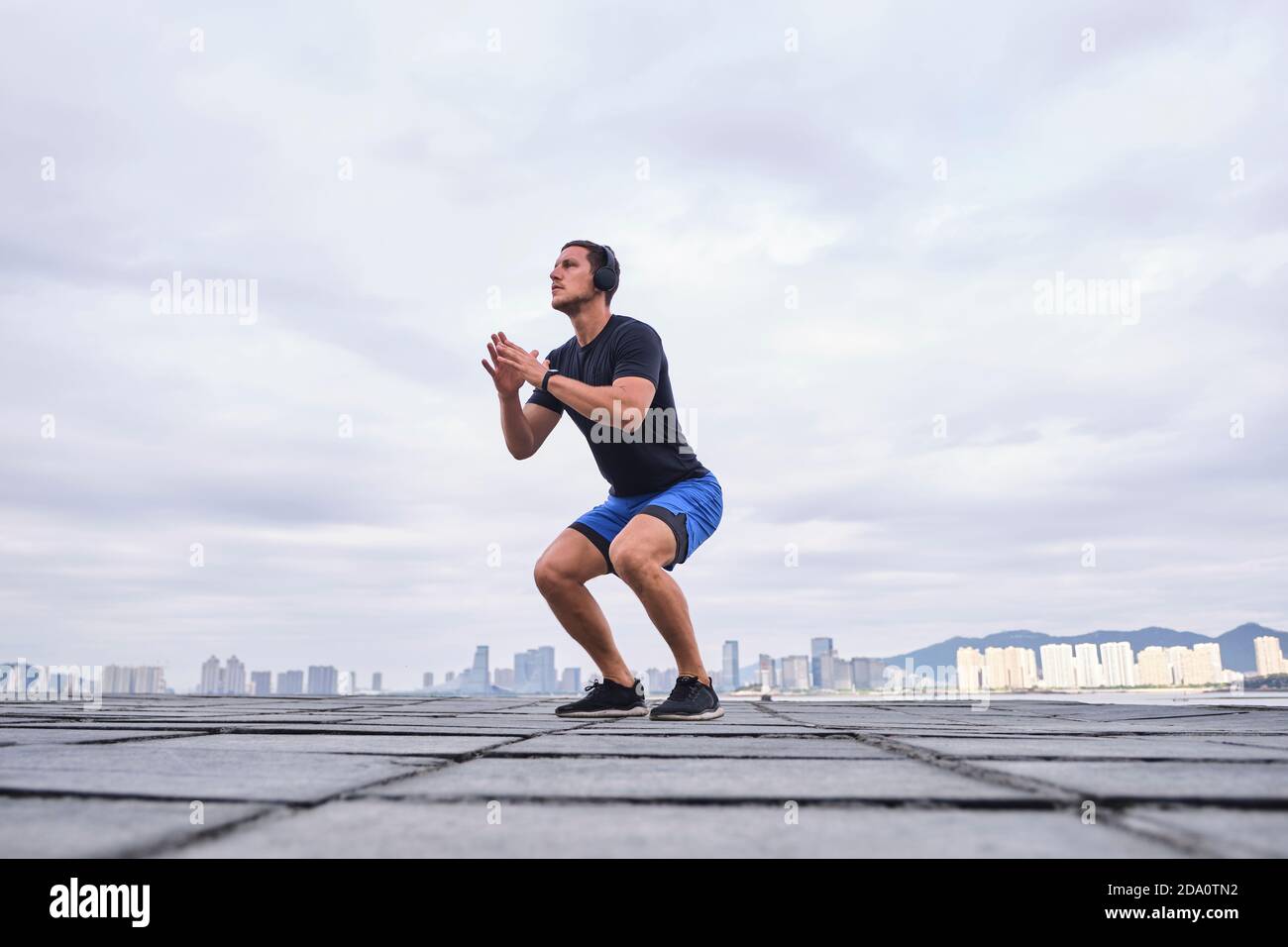 Livello del terreno del corridore energico maschio che riscalda il corpo e. saltare in strada durante l'allenamento cardio mentre si guarda via Foto Stock