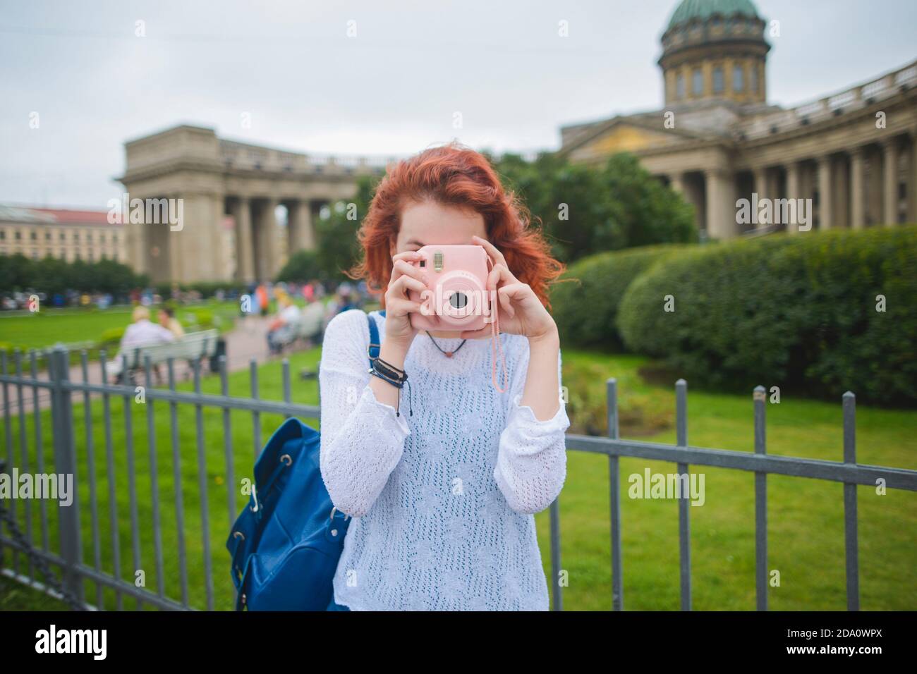 Giovane turista femminile con capelli rossi con zaino che scatta foto con Fotocamera istantanea mentre si è in piedi contro la famosa cattedrale di Kazan in estate Giorno a Saint Foto Stock