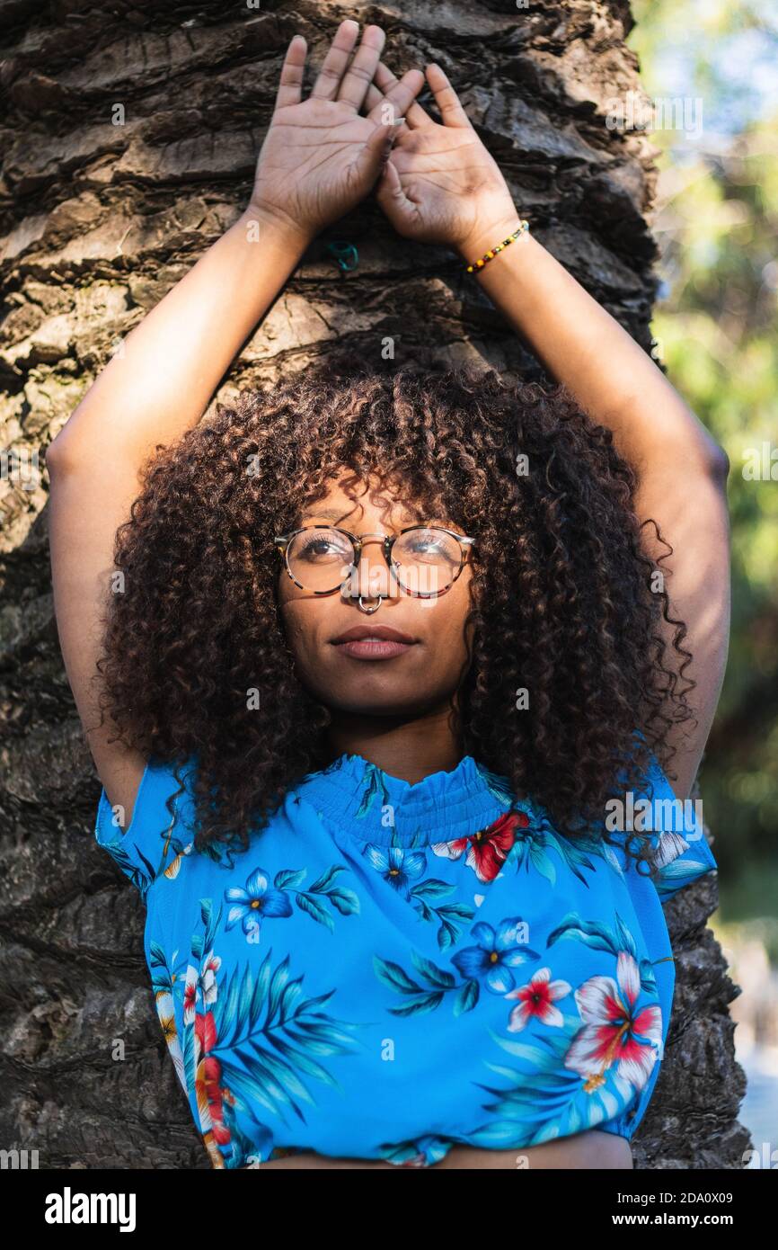 Elegante femmina nera con capelli ricci appoggiati sul fusto del palmo e  guardare via il giorno d'estate Foto stock - Alamy