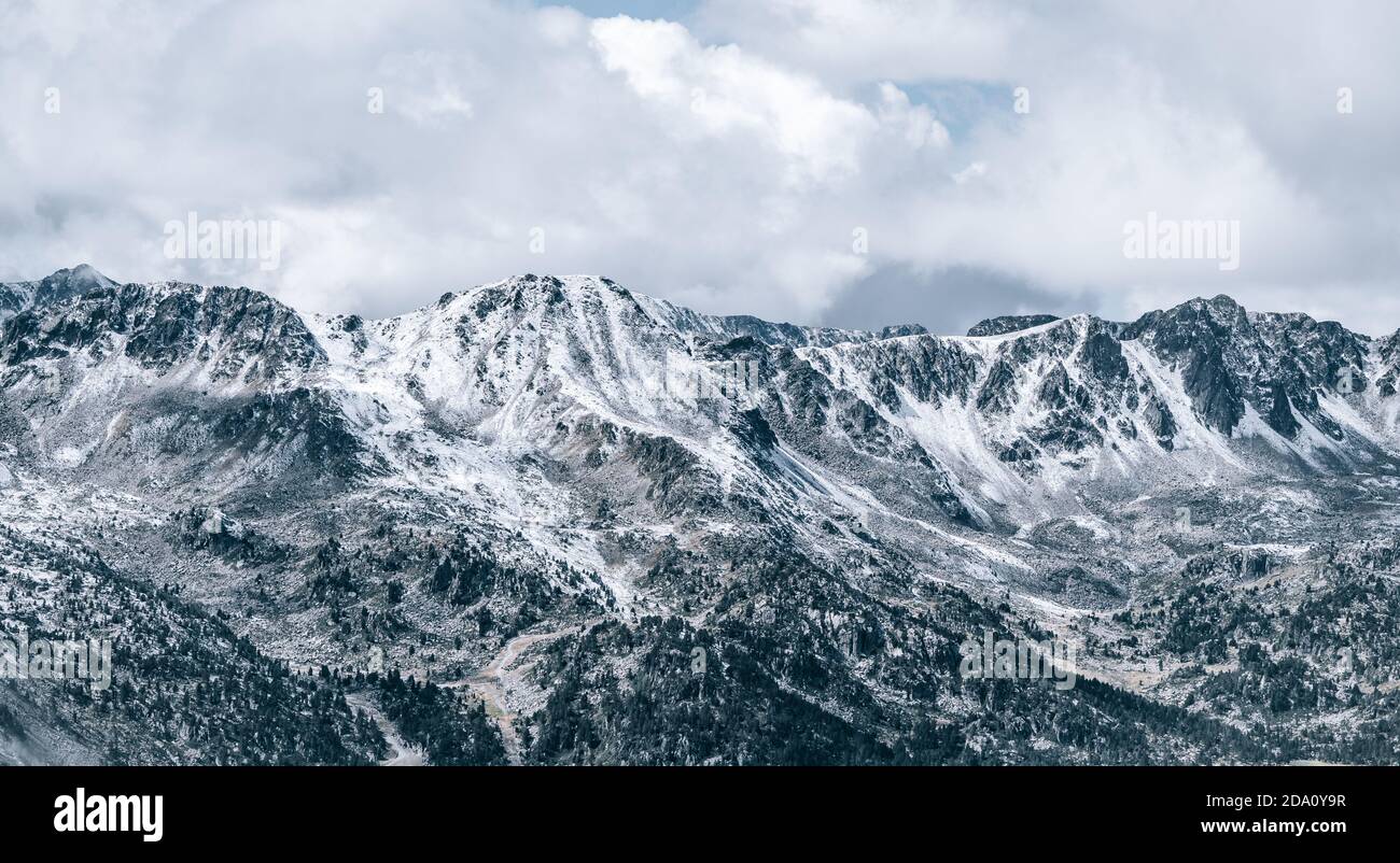 Maestoso scenario panoramico di aspro pendii rocciosi della montagna dei Pirenei Range coperto di neve sotto il cielo nuvoloso in El Pas De la Casa Foto Stock