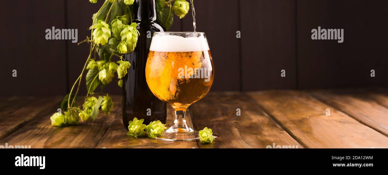 La birra viene versata dalla bottiglia. Birra. Birra leggera Cold Craft in un bicchiere con gocce d'acqua. Pinta di birra da vicino su uno sfondo di legno. Progettazione di bordi. Banner Foto Stock
