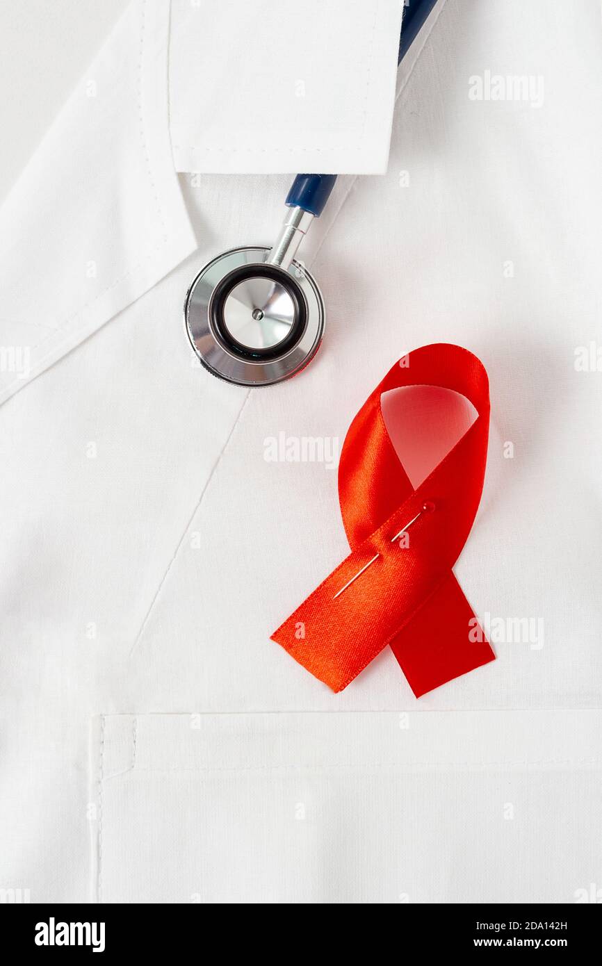 Giornata mondiale dell'AIDS. Nastro rosso come simbolo di questo giorno su uniforme medica bianca. Primo piano. Foto Stock