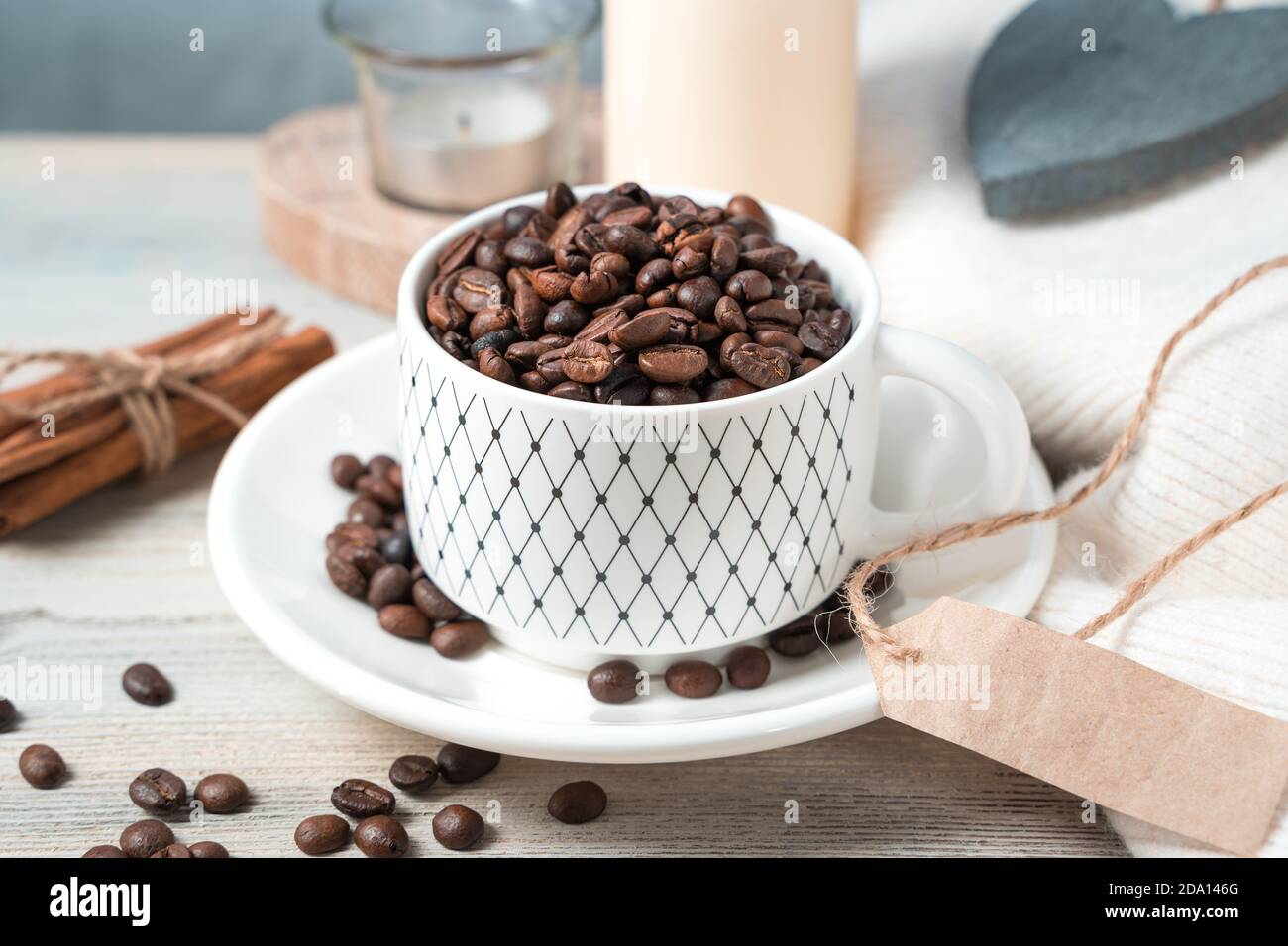 Accogliente sfondo di caffè con chicchi di caffè interi, cannella e candele su uno sfondo di legno chiaro. Foto Stock