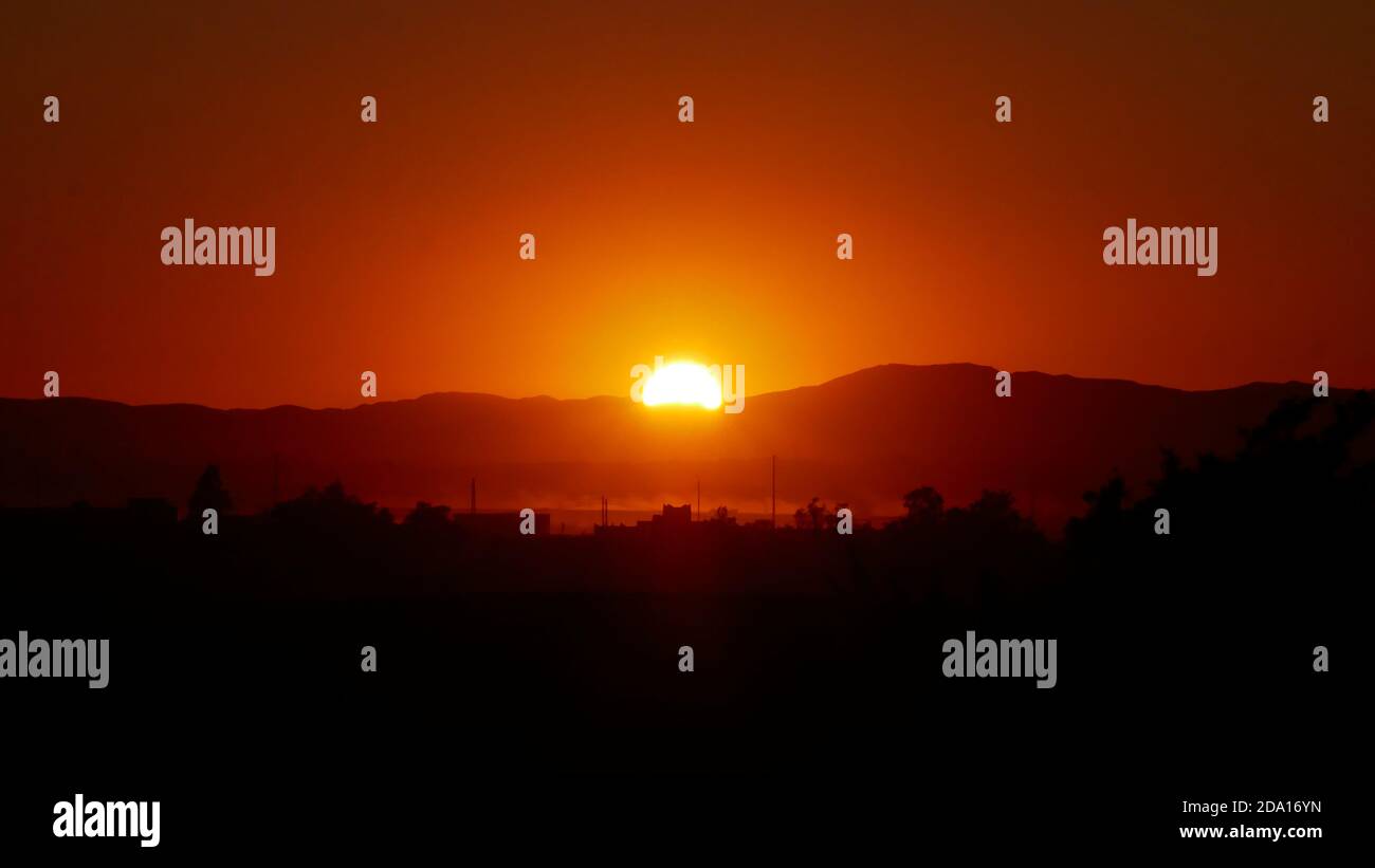 Tramonto mozzafiato con sole luminoso che illumina il paesaggio in colori rosso e arancione sopra la città deserta Merzouga, nel sud del Marocco, Africa. Foto Stock