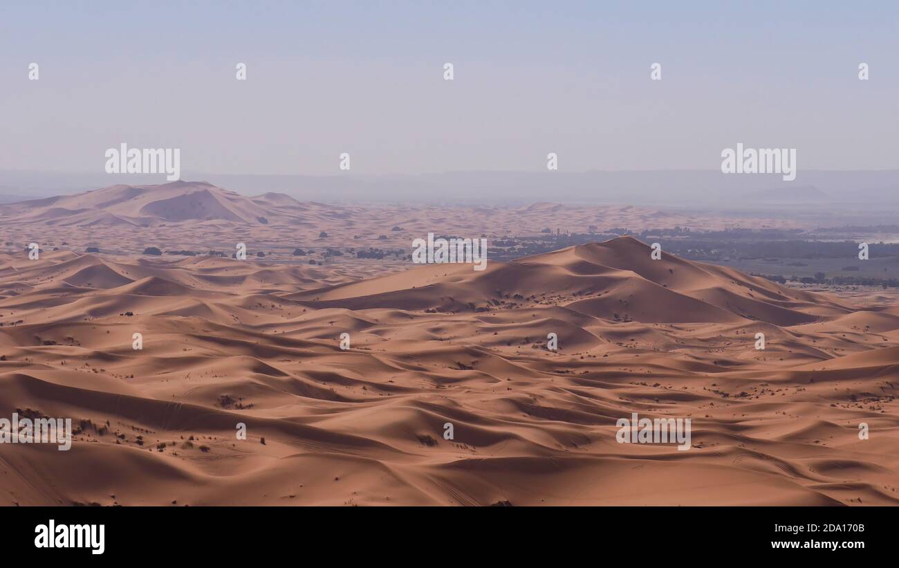 Splendida vista panoramica sulle grandi dune di sabbia del deserto Erg Chebbi con villaggio Merzouga, Marocco, Africa al sole di mezzogiorno con aria frizzante. Foto Stock